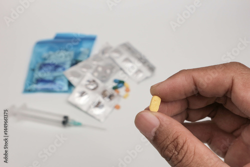 Close-up of a hand holding a single tablet with blurred medical supplies in the background