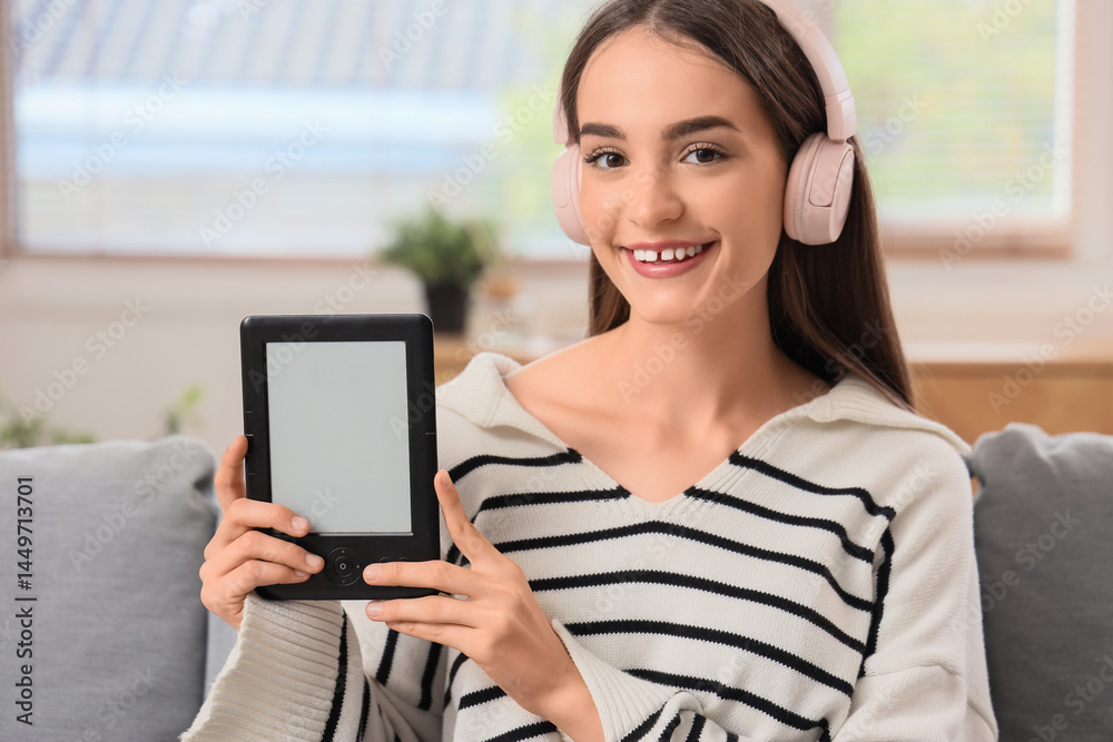 Fototapeta premium Young girl with e-reader sitting on sofa at home