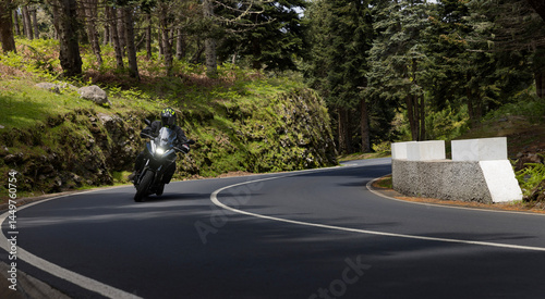 Driver riding motorcycle on empty asphalt road, spring mountains