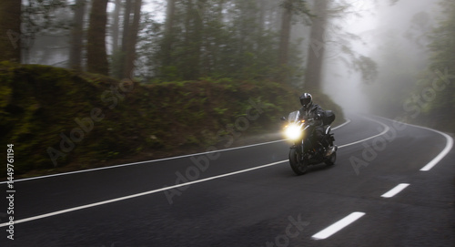 Driver riding motorcycle on empty road , foggy rainforest, spring mountains