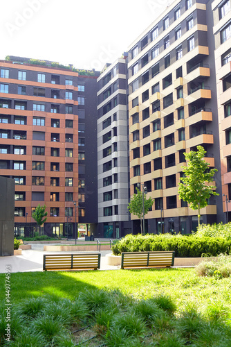 Condominium in a European city: vertical photo of neat multi-storey panel houses with hidden equipment and facilities and a cozy courtyard with trees and benches. Comfortable life in a new district.