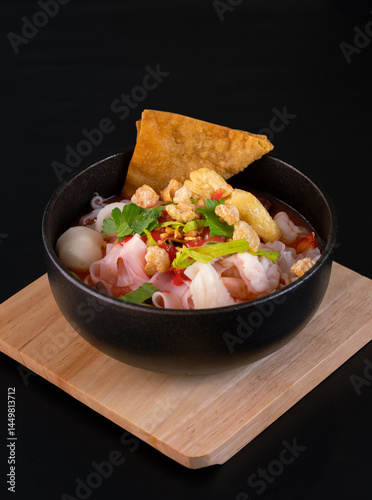 A bowl of Thai traditional pink noodle soup (or Yentafo in Thai) with seafood topping and ingredients such s garlic, and fried crispy dumpling.