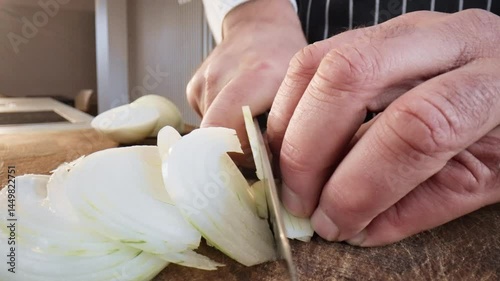 Close-up as a chef expertly chops an onion with a large kitchen knife on a wooden cutting board. Slow motion 50fps.