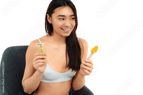 Positive asian young woman holding razor and stick with pasta for depilation photo