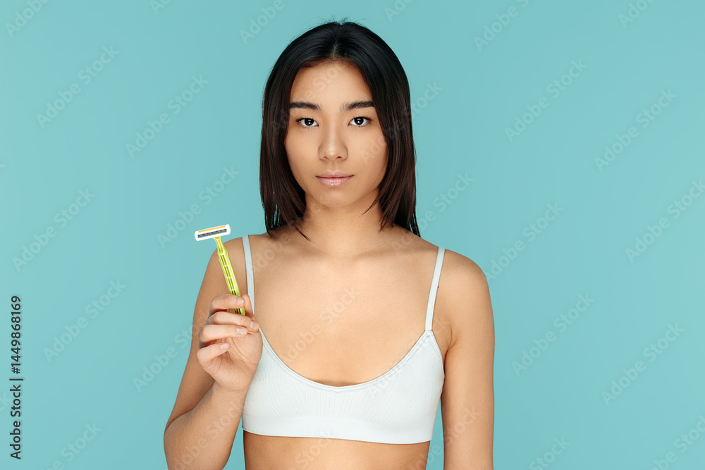 Serious asian woman holding hair removal razor over blue background
