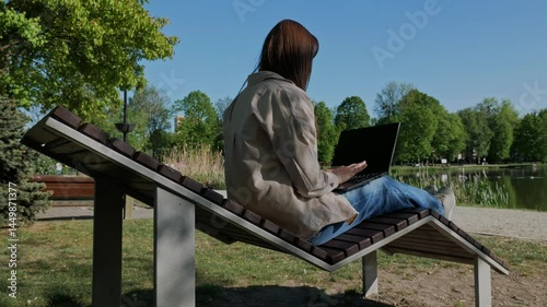 Businesswoman, working on her laptop while sitting on a lounge chair by the lake .