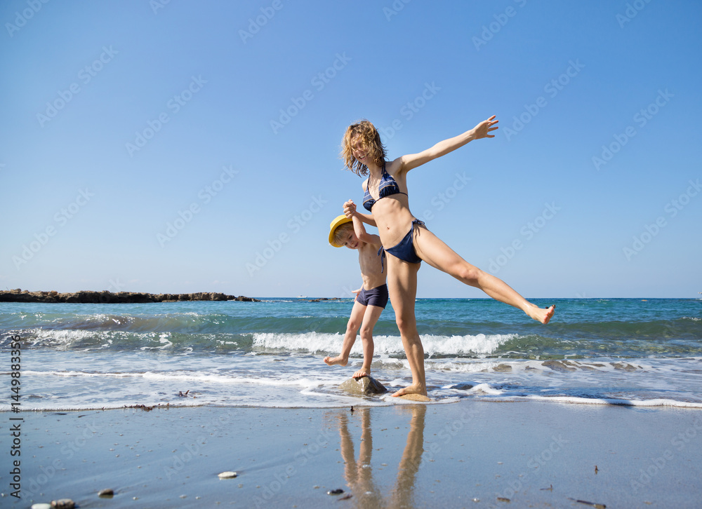 Fototapeta premium Teenage girl and boy 4-5 years old, older sister and younger brother in bathing suits stand in sea, splashing happily in water. Fun time together during holidays, hello summer. Health improvement