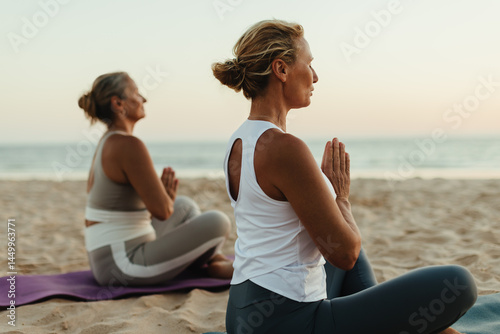 Obraz na plátně Women practicing yoga on a beach at sunset in serene surroundings
