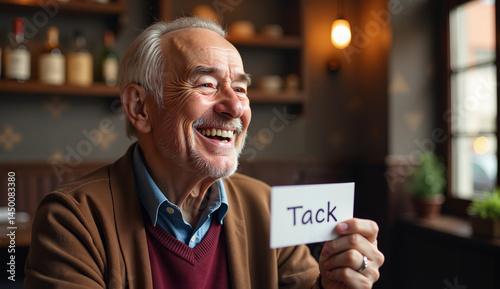 A friendly elderly man holds a thank-you card in Swedish in a warm atmosphere.