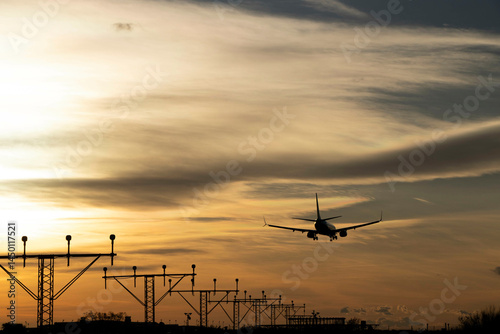 Plane landing, backlit in the sky at a beautiful sunset. A large, beautiful plane. You can see the airport antennas and the runway in the background.