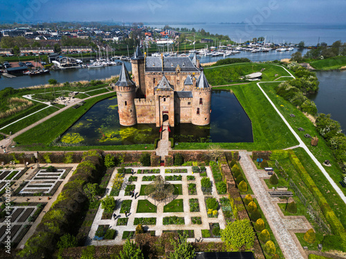 Flying view of Muiderslot Castle on a sunny spring day, showing its medieval structure, gardens, and water defenses.