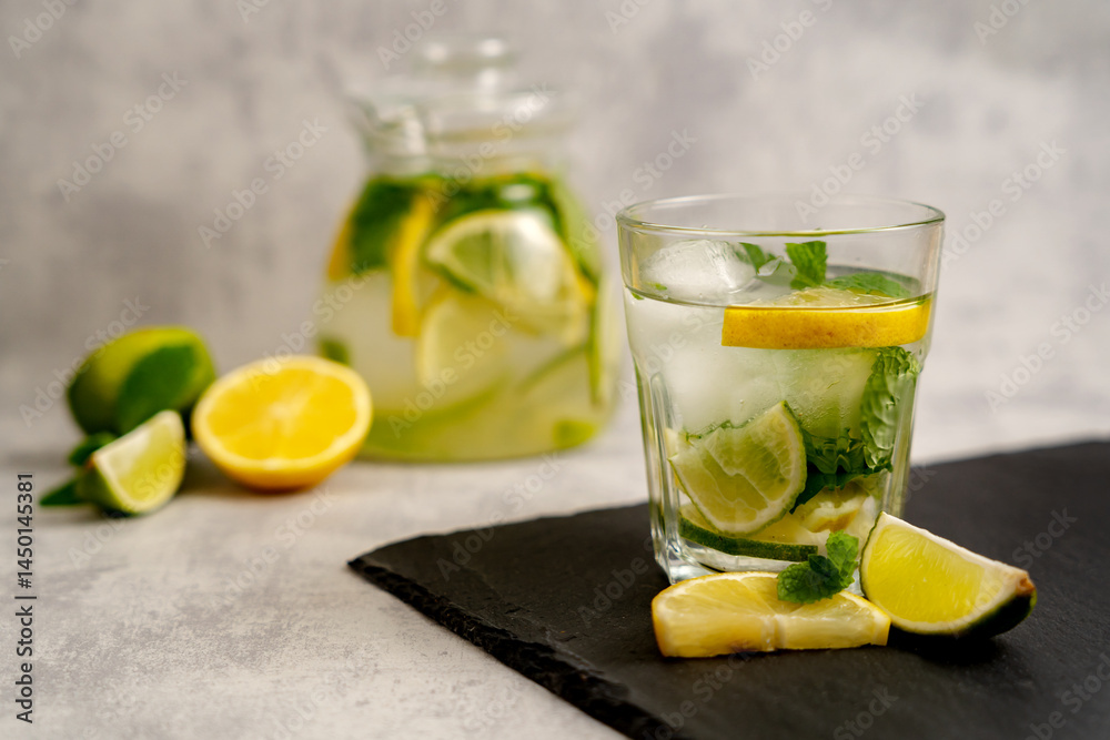 Fototapeta premium Healthy iced tea with lemon and mint with citrus slices on a slate board on a blurred gray background with fruits. Refreshing cold summer lemonade.