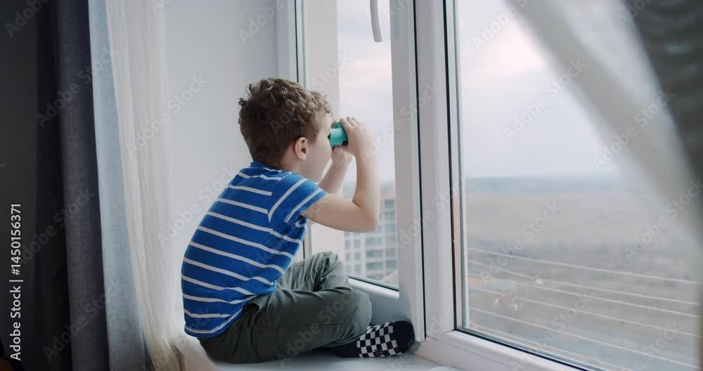 A curious boy gazes out the window, exploring with binoculars