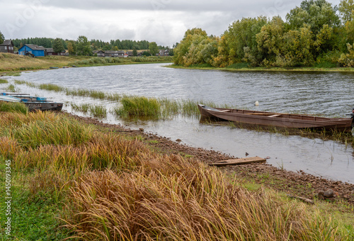 Boats on the river bank against the backdrop of log houses and an old wooden church.