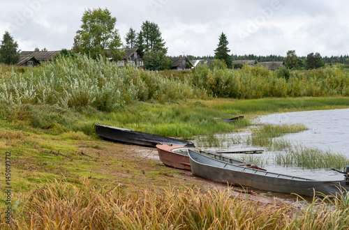 Boats on the river bank against the backdrop of log houses and an old wooden church.
