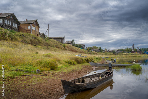 Boats on the river bank against the backdrop of log houses and an old wooden church.