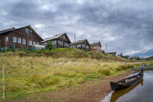 Boats on the river bank against the backdrop of log houses and an old wooden church.