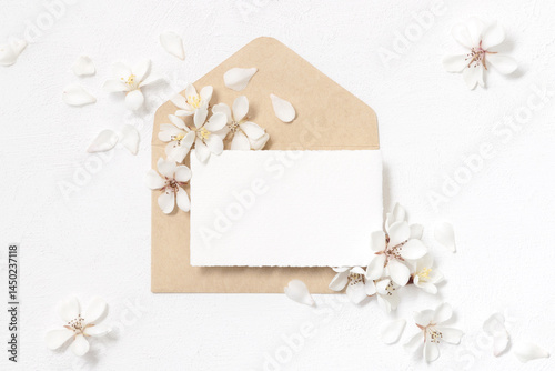Obraz na płótnie Blank paper card over envelope near white cherry flowers top view, spring wedding mockup w salonie