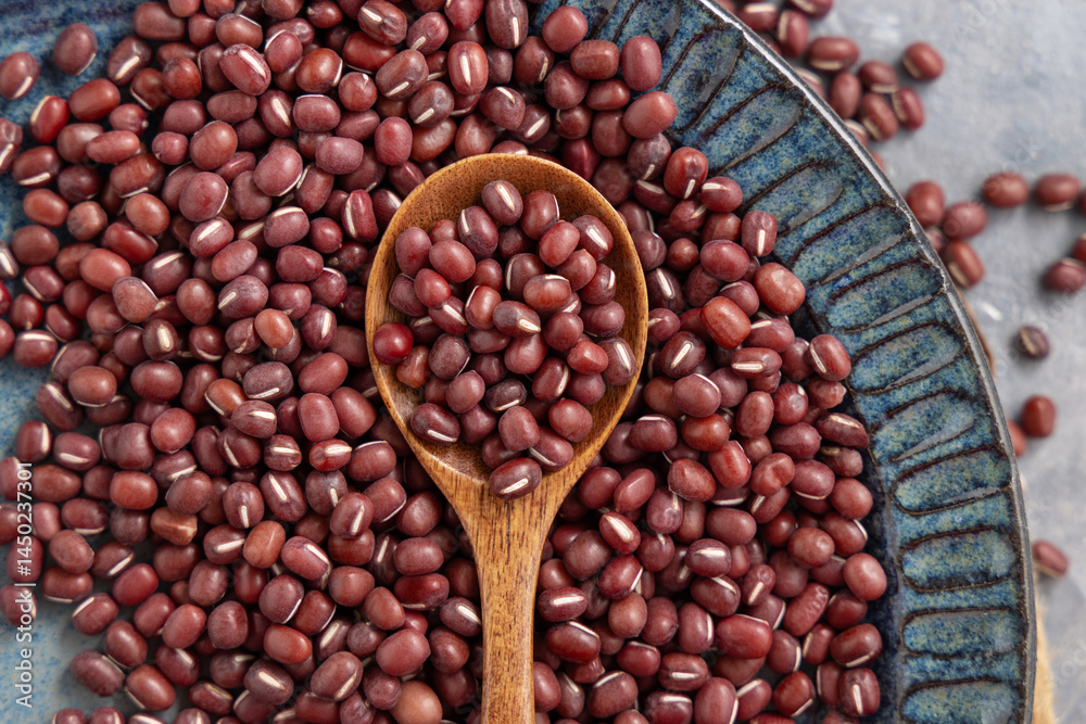 Blue plate full of dried red azuki beans with a wooden spoon top view. Vegetarian protein source