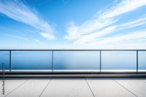 Outdoor balcony overlooking a vast body of water, bathed in sunlight.  A modern railing and paved surface lead to the horizon