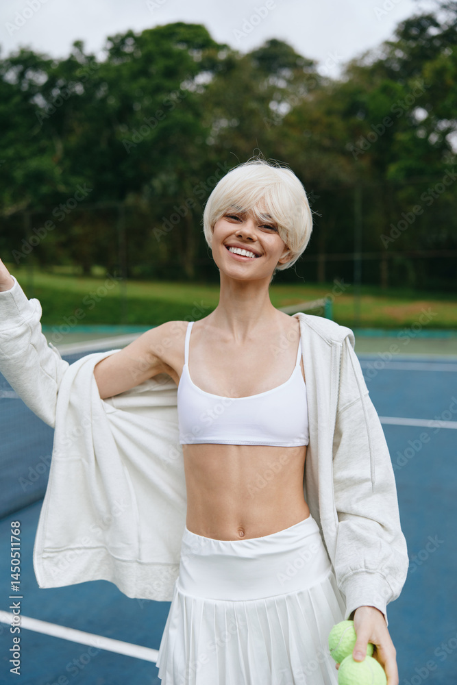 Cheerful young woman with short blonde hair in sporty outfit, smiling on tennis court with green background, embodying a healthy lifestyle and vibrant energy