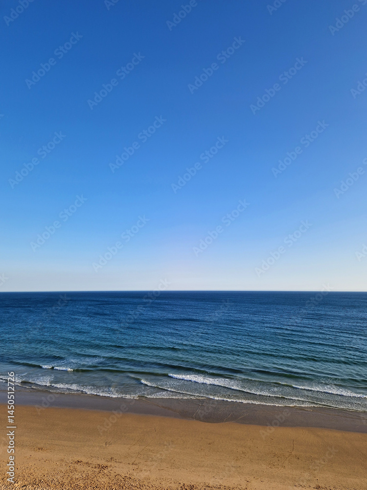 Fototapeta premium Horizon view of a beautiful deserted golden sand beach, ocean waves and blue sky, landscape of Portugal
