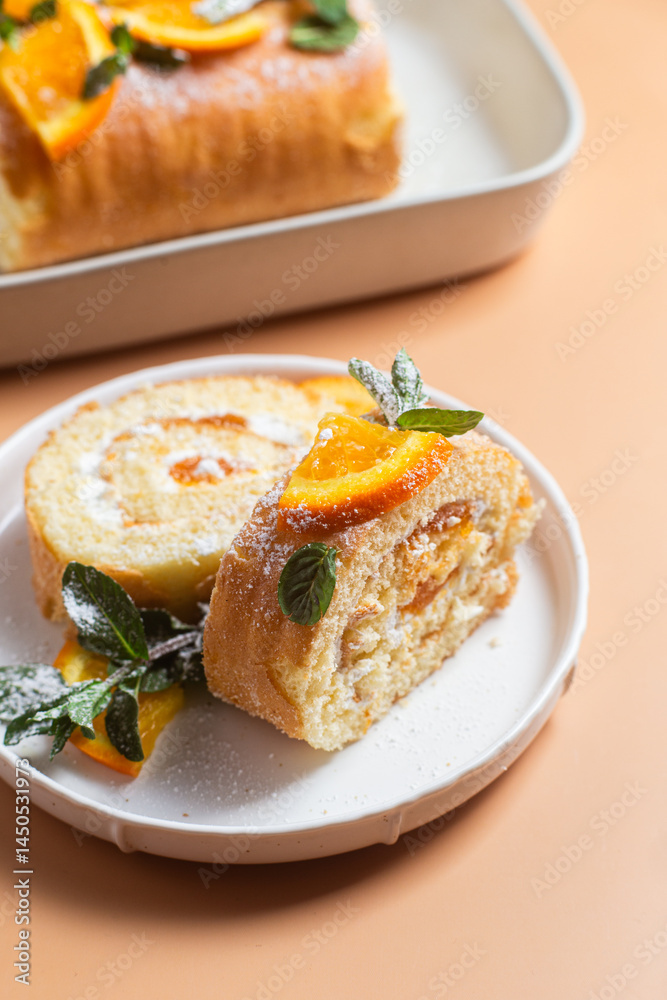 Orange sponge roll with cream and mint in a white plate on a bright background Orange sponge roll with cream and mint in a white plate on a bright background