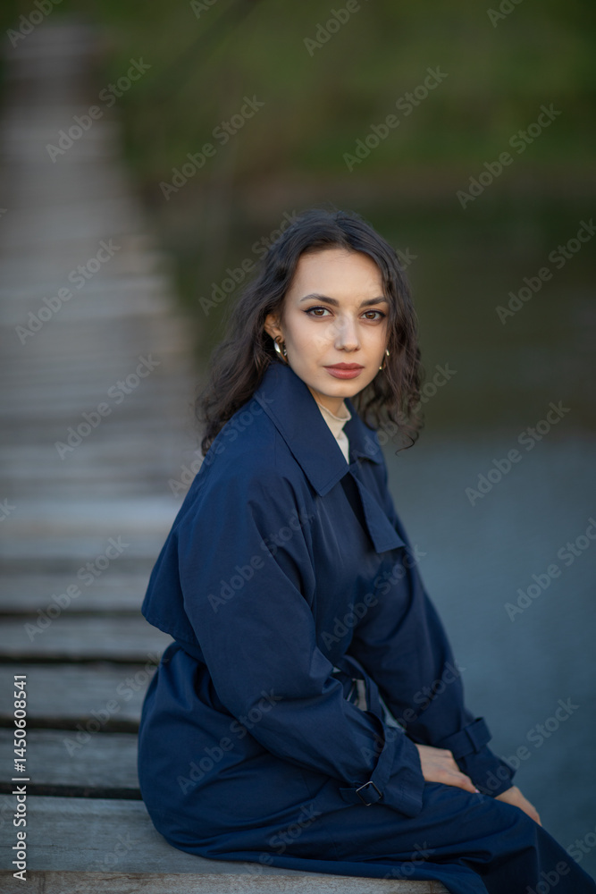 beautiful brunette european girl in blue trench coat at nature. Young lady with beautiful face and lips.
