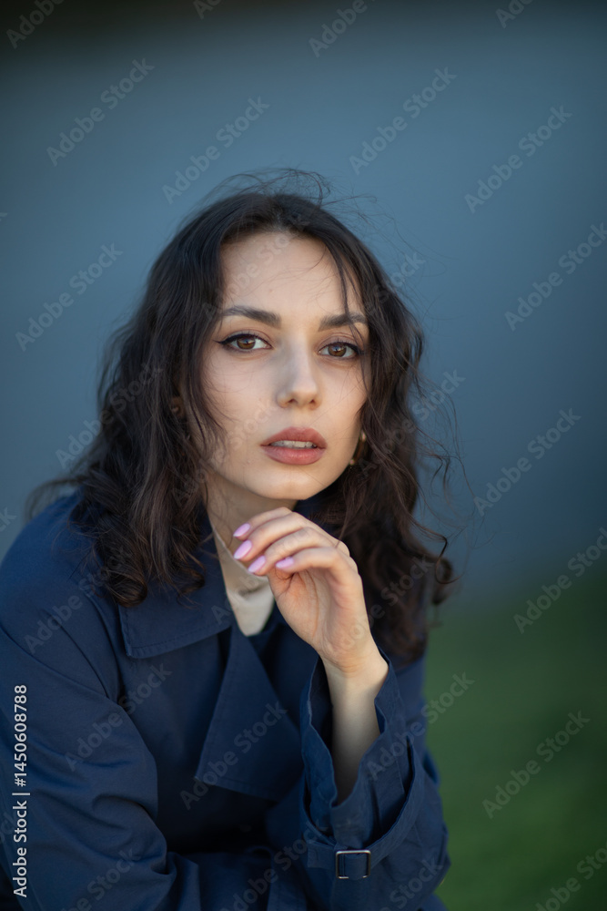 beautiful brunette european girl in blue trench coat at nature. Young lady with beautiful face and lips.