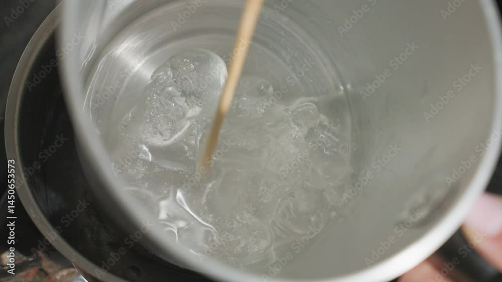 Close up of person stirring soluble mixture inside metal jug placed in steaming pot on gas burner, creating swirling motion in hot water as heat rises during kitchen preparation process Close up of person stirring soluble mixture inside metal jug placed in steaming pot on gas burner, creating swirling motion in hot water as heat rises during kitchen preparation process