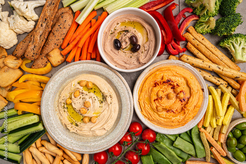 Obraz na płótnie Various hummus dips. Hummus plate with vegetable snacks. Carrot, cucumber, tomato, celery sticks, dry crackers and olive, top view. Vegan and traditional hummus as healthy and vegan snack. w salonie