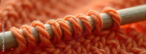 Close-up of orange yarn knitting on wooden needle.