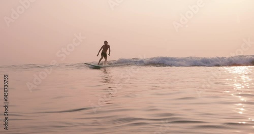 Male surfer on longboard riding on ocean wave with warm sunlight.
