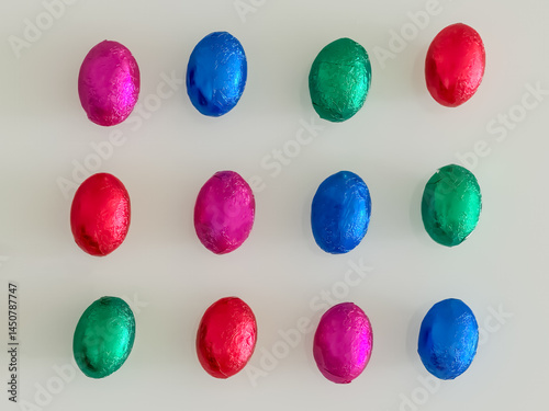 Top view of colorful foil-wrapped Easter eggs arranged symmetrically in rows over a soft light background, perfect for festive design use.