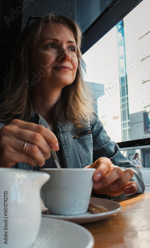 Obraz na płótnie Beautiful woman drinking coffee in cafe. Daily life concept. Enjoy your life concept. Brunette girl stirring milk in americano. Cozy lifestyle. Pretty woman in cafe interior. Coffee break time. w salonie