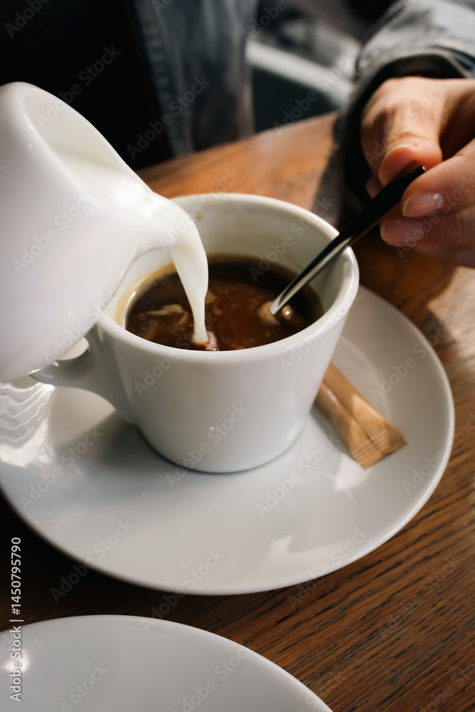 Girl pouring milk to coffee cup. Hands stirring milk in coffee with a spoon. Latte in cafe. Espresso with milk. Hot drinks concept. Relax with coffee. Breakfast concept. Woman in cafeteria.