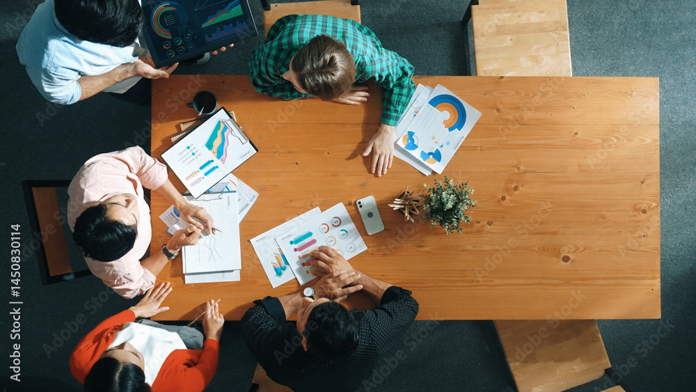 Top view of business man using tablet display increasing graph while diverse marketing people sharing idea or planing strategy at meeting table with stock market statistic scatter around. Convocation.