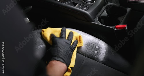 car interior cleaning and detailing service. man cleaning black leather seat with foam spray detergent and microfiber cloth