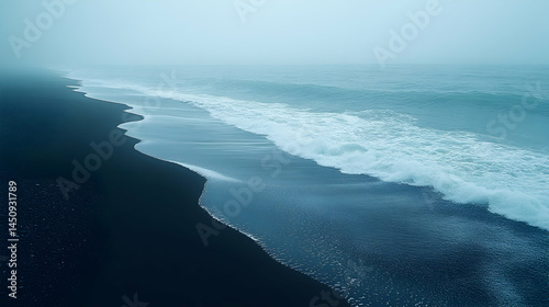 Misty black sand beach meets the ocean waves. Dark sand stretches to a misty ocean.  Waves crash gently