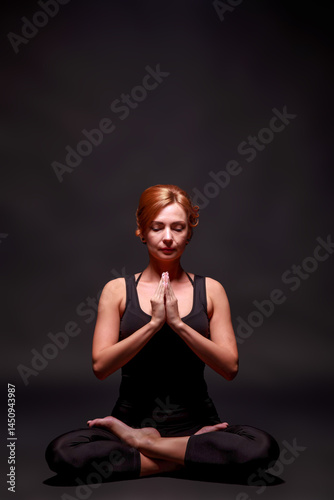 Young slim athletic girl with red hair in black mauka and black shorts doing yoga on black studio background
