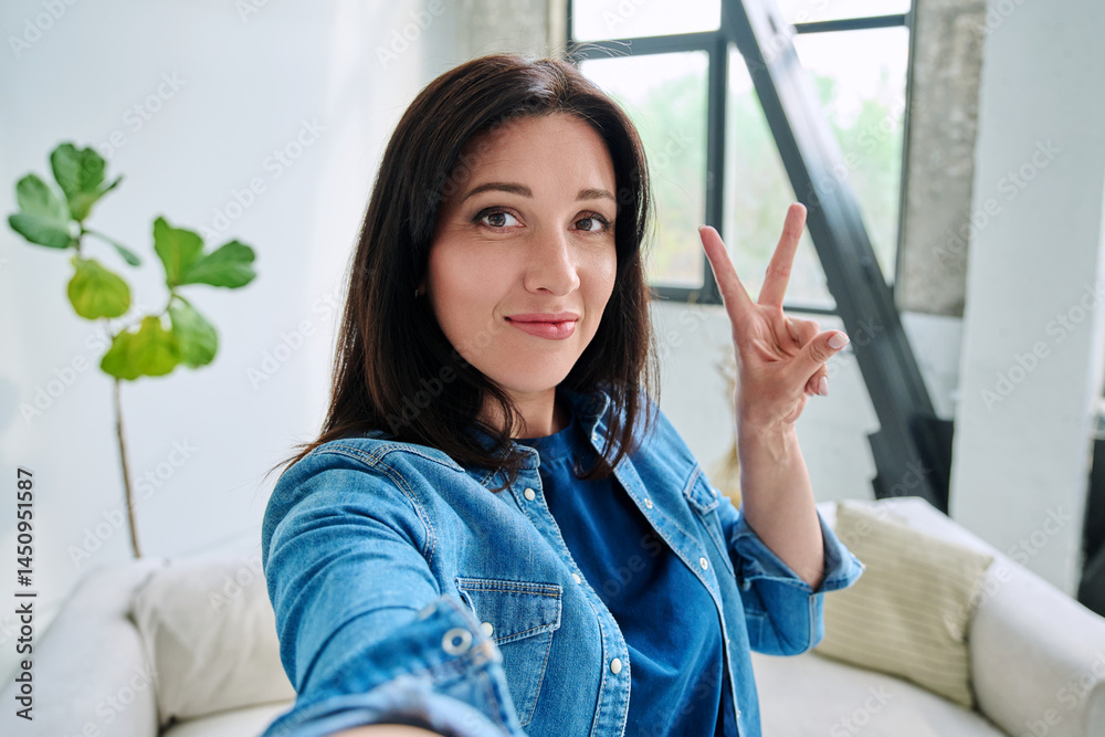 Selfie portrait happy beautiful woman making gesture victory success in home