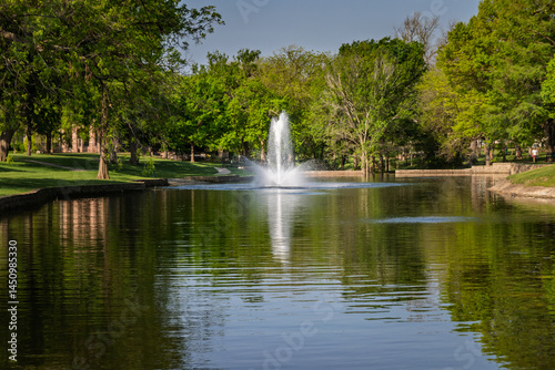 Scenic Wide View of a Water Fountain and Lush Green Trees Reflected on a Calm Pond in Plano Texas