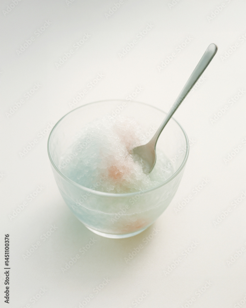 Pastel shaved ice dessert in glass bowl with spoon and melting texture