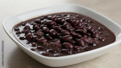 Traditional cooked black beans served in a ceramic bowl over a light, neutral background. Staple Brazilian food, ideal for homemade meals and rustic culinary visuals.