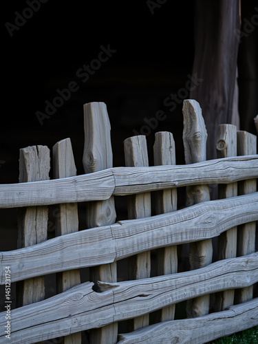 A stockade of rough planks in the village. The background is made of dark wooden boards. A fence in the village.