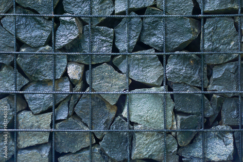Stacked dark stones held in a metal wire grid form a gabion wall used for structure and design.