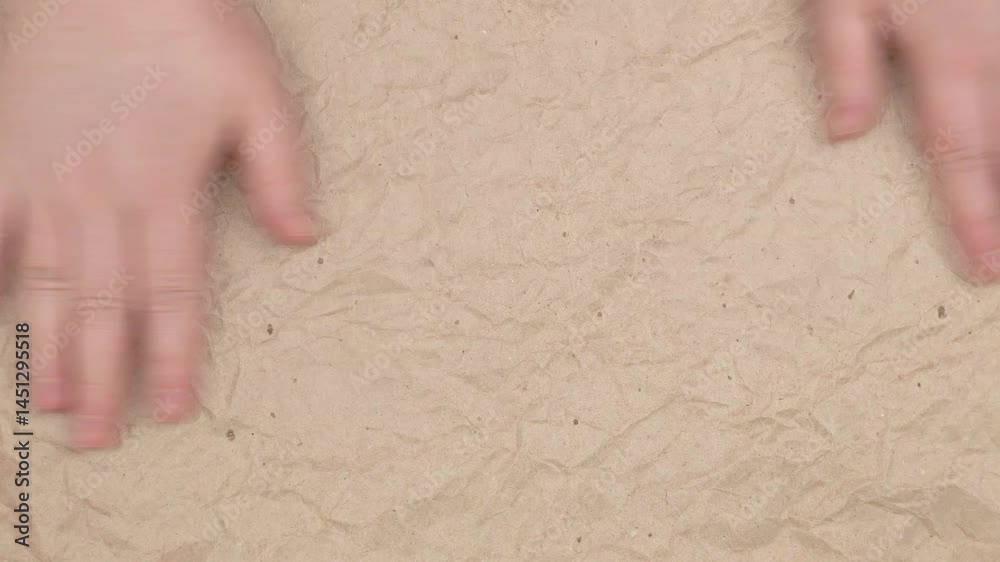 Smoothing wrapping paper with your hands.
Close-up of hands smoothing a sheet of brown wrapping paper on a flat surface. The paper looks wrinkled, creating an interesting texture.
