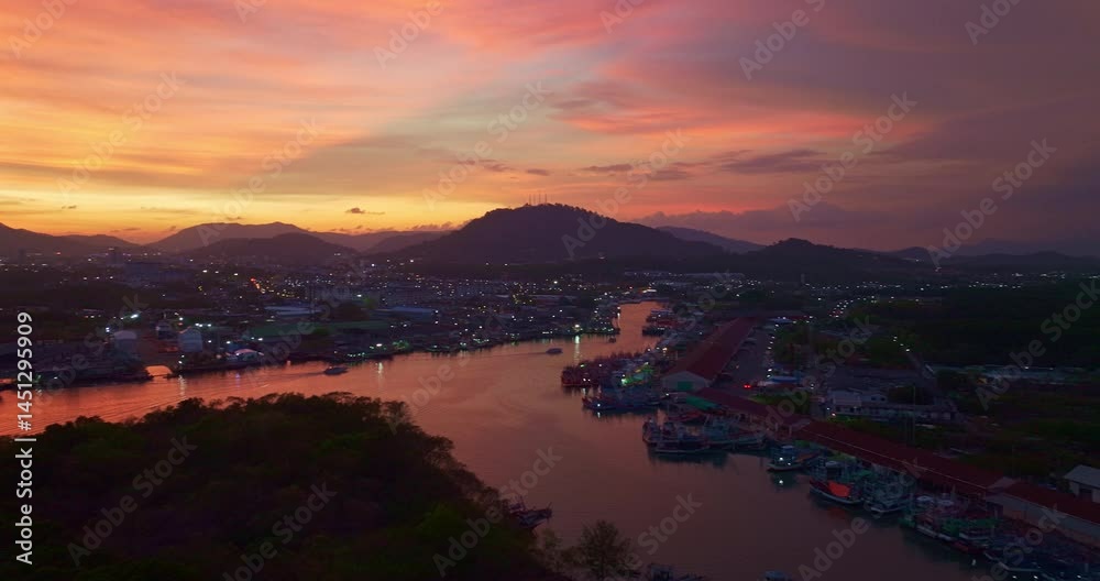 Aerial view of Stunning sunset featuring fishing port in Phuket. The vibrant sky transitions from soft purples to fiery orange hues, creating a tranquil and picturesque atmosphere. Aerial view of Stunning sunset featuring fishing port in Phuket. The vibrant sky transitions from soft purples to fiery orange hues, creating a tranquil and picturesque atmosphere.
