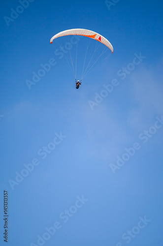 Obraz na płótnie A paragliding athlete is floating in the air showing his skills in controlling a paraglider against a backdrop of bright blue sky. w salonie