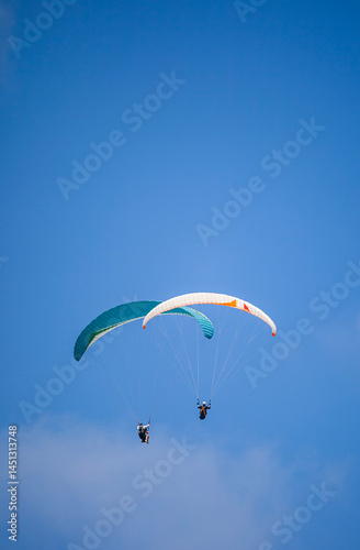 Obraz na płótnie A pair of paragliding athletes are floating in the air showing their skills in controlling their paraglider against a backdrop of bright blue sky. w salonie